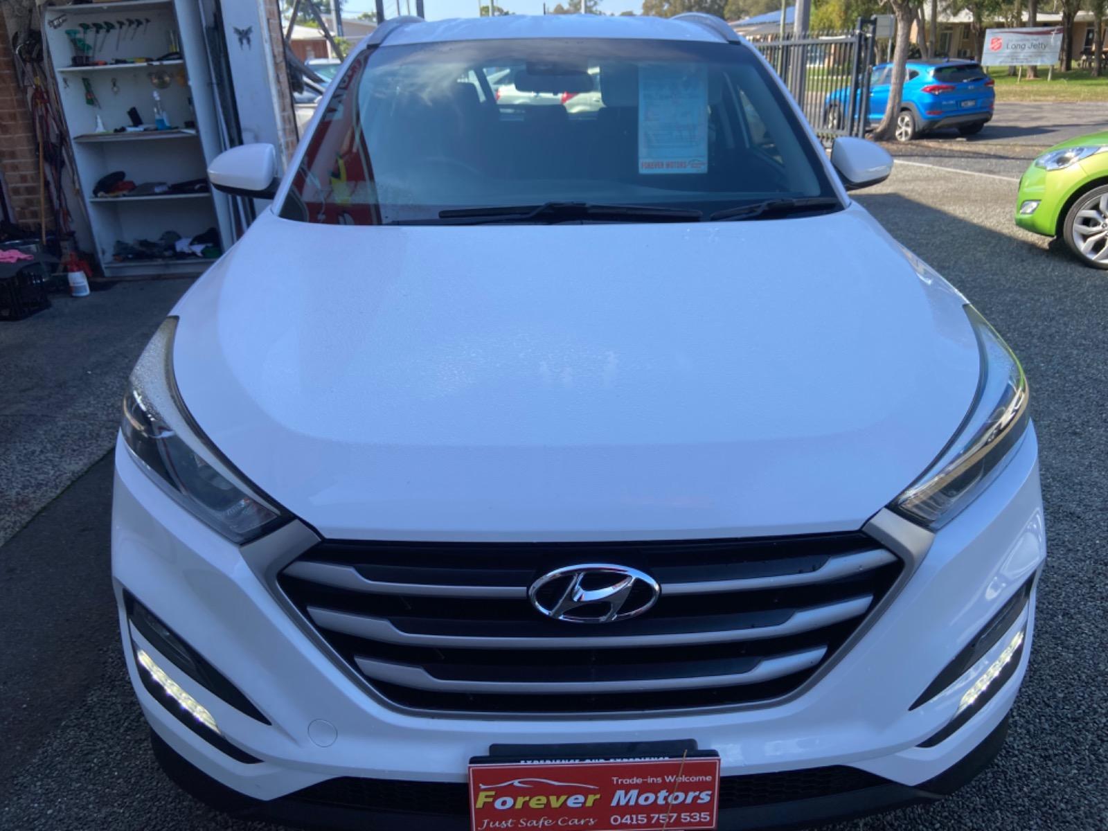 A white Hyundai Tucson on the Forever Motors forecourt wearing the yard's own number-plate surround, other stock and the street behind